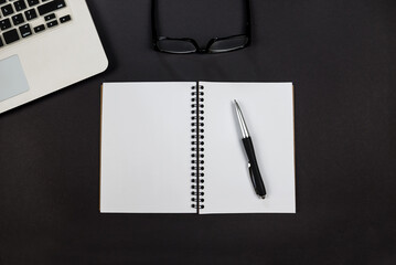 Top view photo of laptop with notepad, pen and glasses on isolated black background.