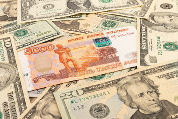 Russian national currency on top of US dollar banknote, top view of mixed rouble banknotes. Russian and American paper money. Rubles and US dollars exchange rate.