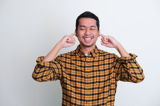 Adult Asian man smiling with eyes closed while covering his ears with finger