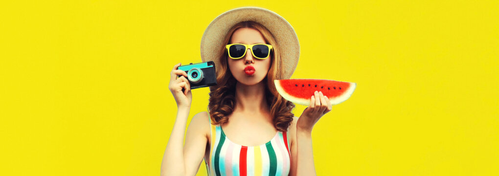 Summer portrait of stylish young woman with film camera and slice of fresh watermelon wearing straw hat posing on yellow background