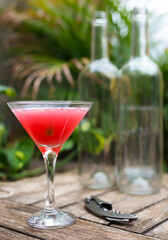 red cocktail with ice in glass with stem on wooden surface