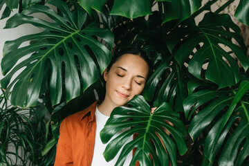 A close-up portrait of the face of a beautiful young woman covering her face with a green monstera...