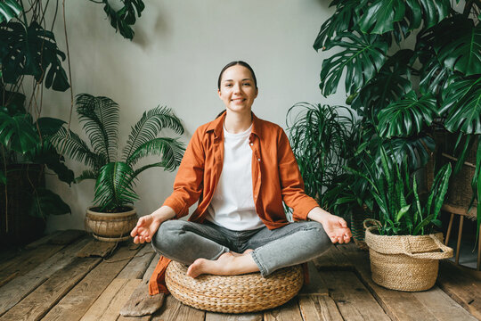 A beautiful young woman is sitting in meditation in the lotus position in a beautiful green garden among the plants of the house. The concept of mindfulness, psychological and mental health.
