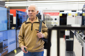 elderly man choosing TV in showroom of electronics store