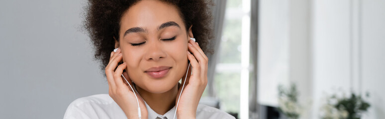 happy african american woman with closed eyes listening music in wired earphones, banner.