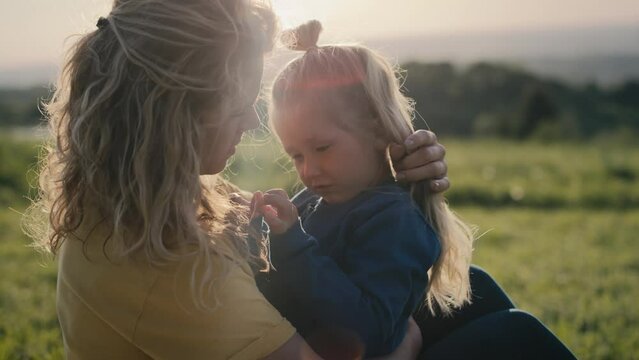 Mom with little daughter sitting on the meadow and bonding together. Shot with RED helium camera in 4K.   