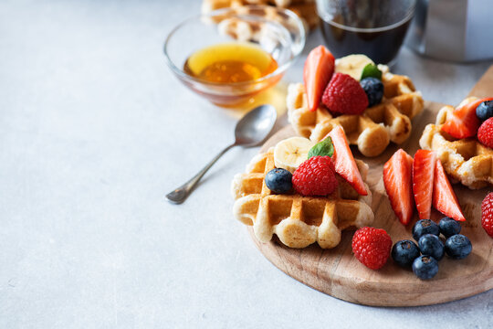 Waffles with berries and honey and coffee on a wooden board. Close up and copy space. Breakfast or brunch concept.