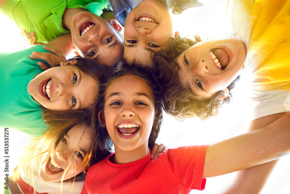 Wall mural Bunch of cheerful joyful cute little children playing together and having fun. Group portrait of happy kids huddling, looking down at camera and smiling. Low angle, view from below. Friendship concept