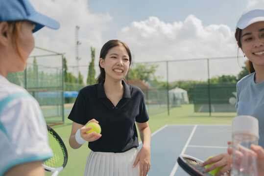 Happy asian young friendship talking and resting after match on the outdoor tennis court on a bright sunny day.