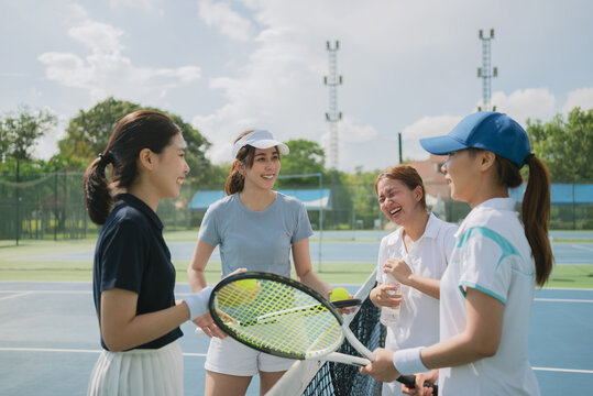 Happy asian young friendship talking and resting after match on the outdoor tennis court on a bright sunny day.