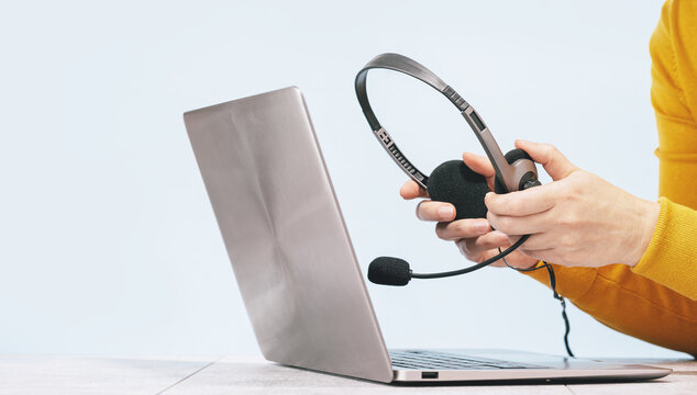 Laptop. headphones or headset on desk and plain background. Female hands over laptop. Distant learning or working from home, online courses or support concept. Helpdesk or call center operator