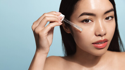 Close up of young asian woman with beautiful skin. Female model with fresh and healthy skin looking at camera. Girl with dropper applies serum, collagen and argan oil moisturizer