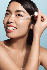 Beauty collagen. Vertical of beautiful asian woman applies C-serum, tea trea argan oil skincare treatment, daily care skin regime, blue background