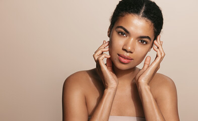 African american woman with clear, glowing facial skin, touches her face with tender gaze,...