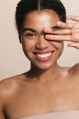 Vertical of dark skinned model shows her glowing, clear natural facial skin, covers her eye with...