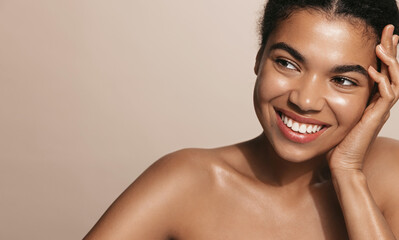 Smiling young woman with glowing facial skin, touching her perfect nourished face, brown background