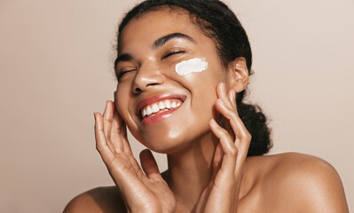 Smiling woman using skincare product. Female taking face cream to apply on facial skin - obrazy, fototapety, plakaty