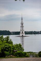 an old white high bell tower in the middle of the river against the background of the forest on a...