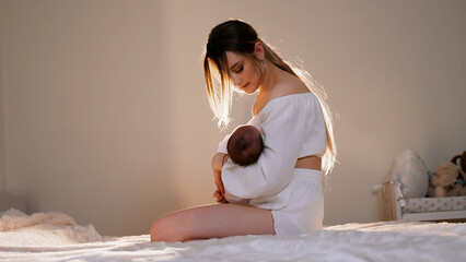 Mother holds newborn baby in her arms and gently strokes it. Woman admires child. Beautiful happy...