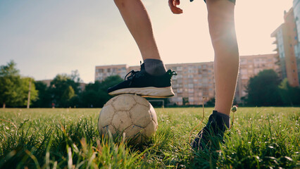Teenager guy in the stadium. The guy stands on the grass and keeps his foot on the old soccer ball close up. Outdoor sports. Young football player in sneakers and shorts. Sports game with a ball.