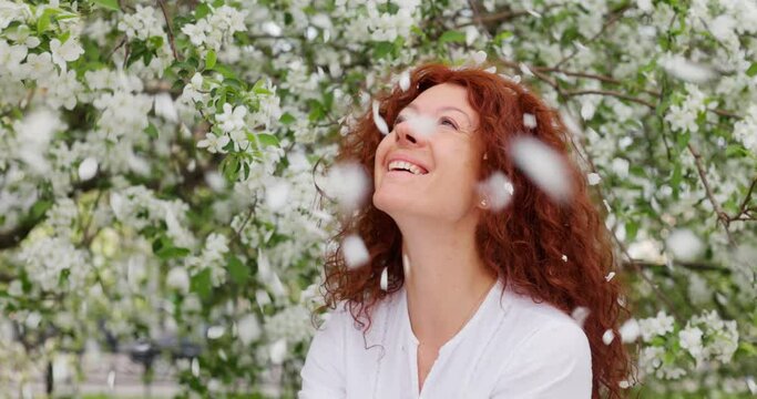 Red-haired woman looking at the camera and smiling in a blooming apple orchard