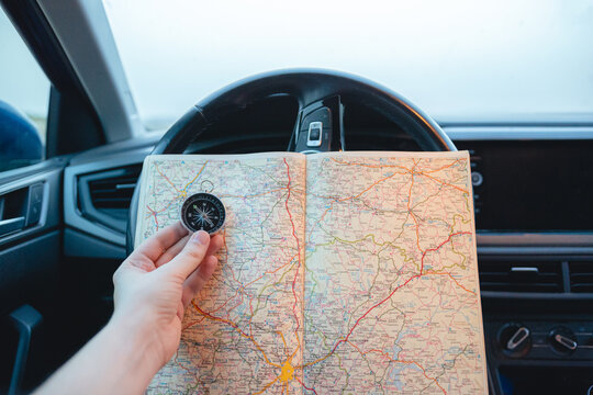 Close-up of a man with a compass and a map in his hands inside of a car