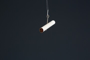 Isolated shot of a cigarette hanging on a hook on a black background. Cigarette addiction concept
