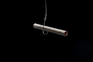 Isolated shot of a cigarette hanging on a hook on a black background. Cigarette addiction concept