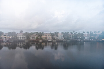 Fototapeta premium Cloudy foggy mist morning in Hollywood Beach in Miami, Florida Stranahan river and view of waterfront villas houses with palm trees and calm water reflection