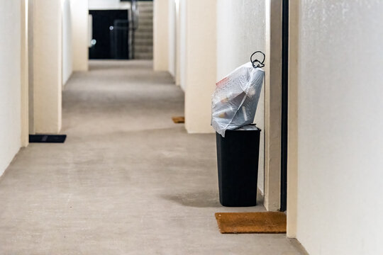 Concierge valet door to door trash collection services for apartment with garbage in bin and plastic bags for pick up in residential building hallway corridor hall