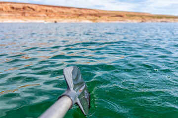 Kayaking in Lake Powell towards antelope canyon with closeup of paddle oar by blue color water surface and rock formations in background point of view