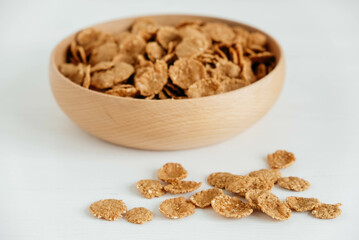 Crispy healthy dry cereal flakes in a wooden bowl on white background