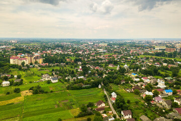 Aerial landscape view of village houses and distant green cultivated agricultural fields with growing crops on bright summer day