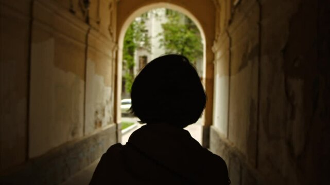 silhouette of a beautiful girl passing through the arch in the central part of the city of Kyiv. bob hairstyle back view. Slow Motion 100fps 2.8k