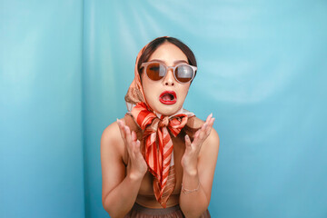 Retro concept of a young Asian woman expressing her sad hysterical face isolated by a blue...