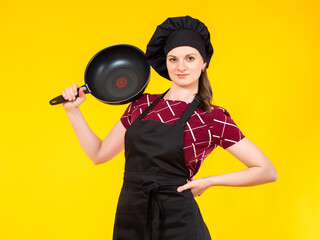 Cook hides his face behind a saucepan. Portrait of a female chef with a saucepan in front of her face. Cook tries to hide. Girl chef on a yellow background. Cook in a black chef's hat.