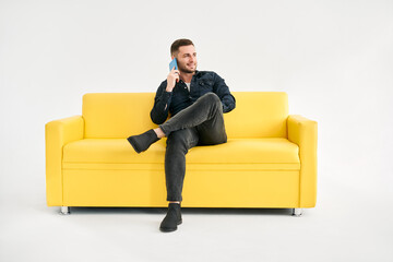 Smiling relaxed man talking on the phone while sitting on yellow sofa