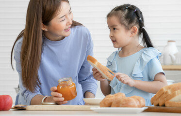 Happy Asian family, cute little daughter and young mother are spreading jam on sliced bread...