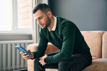 Relaxed man sitting on couch using hsi mobile smart phone