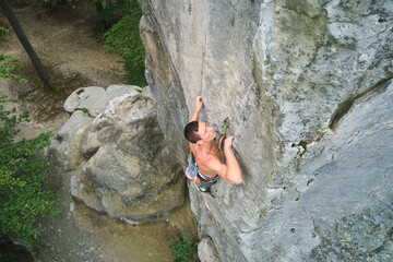 Young man climbing steep wall of rocky mountain. Male climber overcomes challenging route. Engaging in extreme sport concept