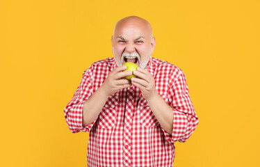 hungry old aged man in checkered shirt eat apple on yellow background