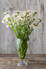 A bouquet of daisies in a transparent vase on a wooden table. Light wooden background