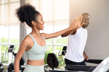 Black African American couple clapping hands together while running on the treadmill at fitness club. Healthy lifestyle, training in gym. Fitness partners give a high five. healthy concept.