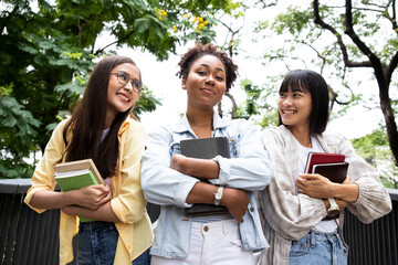 Portrait of a diversity woman student holding books and looking at natural outdoors with friends at park. Prepare for college and university concept