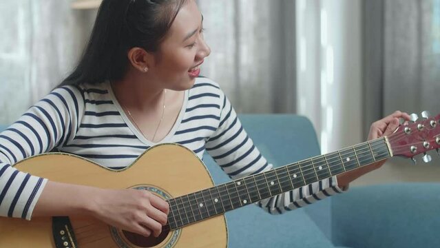 Close Up Of Asian Woman Learning Pulling Strings Of Guitar By Laptop At Home

