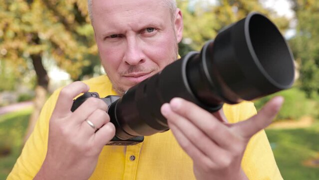 Video, an adult man makes a photo on a camera with a large lens. In the street on a sunny day in summer.