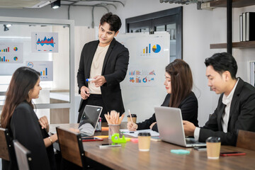 An Asian businessman is presenting his company performance report to his boss or group of male and female colleagues with confidence and professionalism.