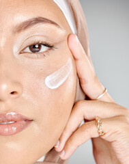 Portrait of a young Muslim woman wearing a hijab or headscarf applying a cream moisturizer on her flawless skin while showing her eyelash extensions while. Applying cosmetics to maintain healthy skin