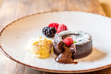 Chocolate fondant (cupcake) with raspberries, ice creme and powdered sugar placed on plate