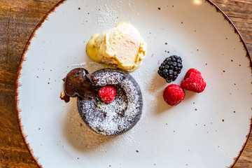 Chocolate fondant (cupcake) with raspberries, ice creme and powdered sugar placed on plate